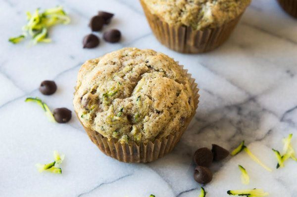 zucchini chocolate chip muffins sitting on a marble surface with chocolate chips and shredded zucchini scattered about