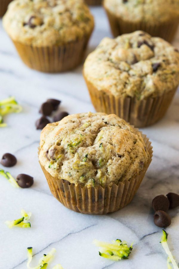 zucchini chocolate chip muffins sitting on a marble surface with chocolate chips and shredded zucchini scattered about