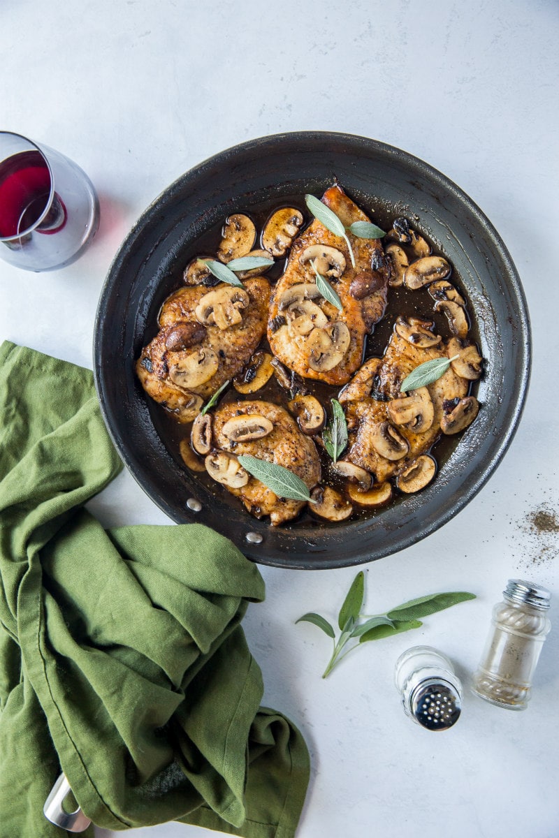 chicken marsala in a skillet with a glass of red wine, a green cloth napkin and salt and pepper shakers