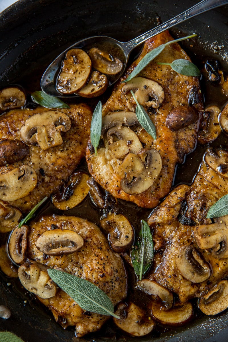 Chicken marsala in a skillet garnished with fresh sage