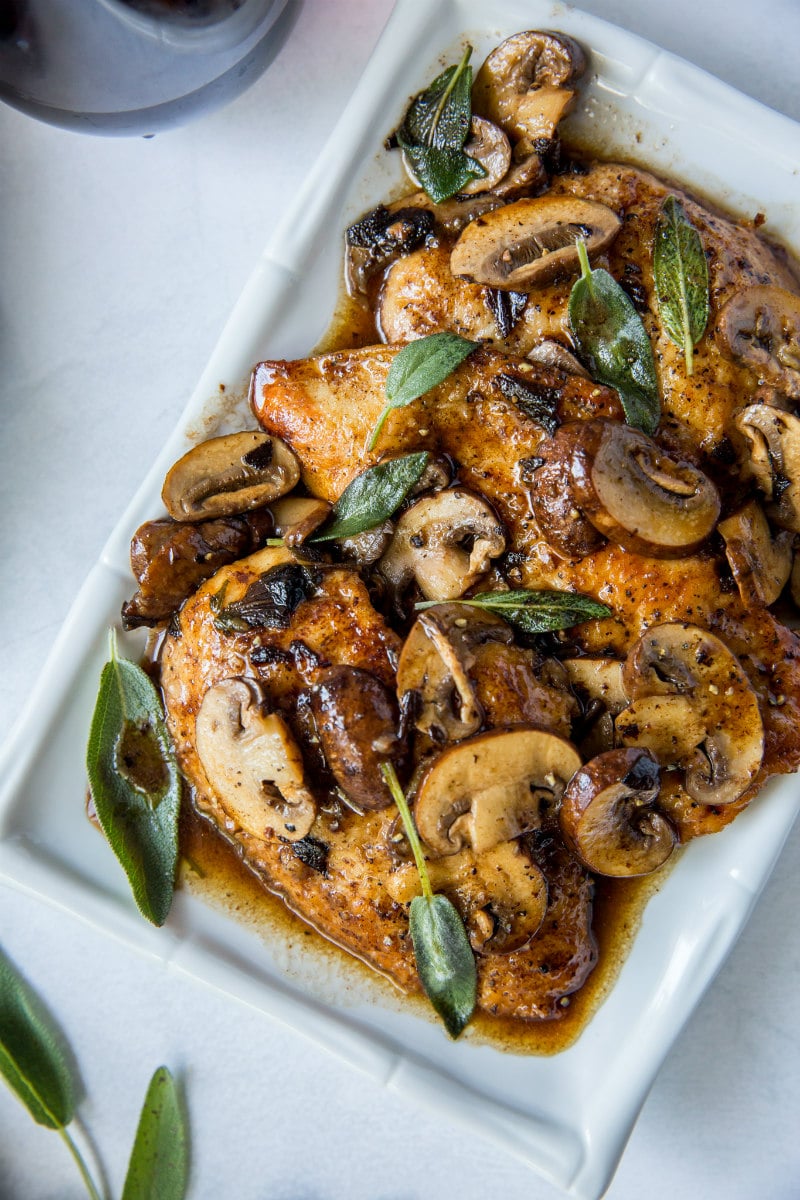 chicken marsala garnished with fresh sage on a white platter