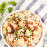 ensalada de patata con tocino y queso azul en un tazón blanco con servilleta de tela a rayas azules y blancas con guarnición de perejil