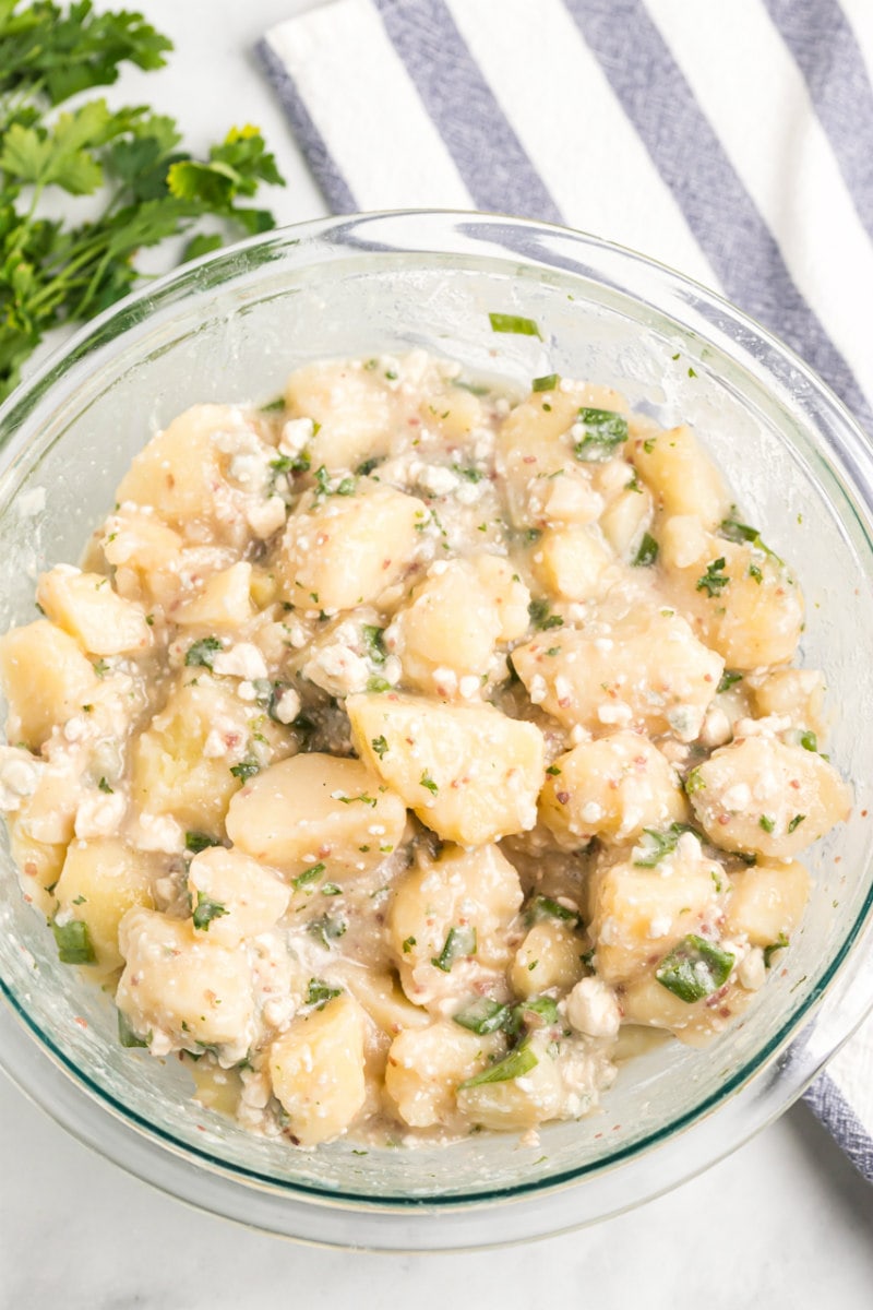 blue cheese potato salad in a glass bowl displayed on a white and blue striped napkin with parsley garnish