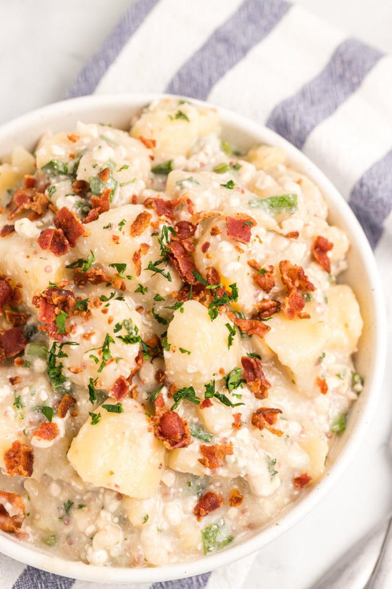 blue cheese and bacon potato salad in a white bowl displayed on a white and blue striped napkin