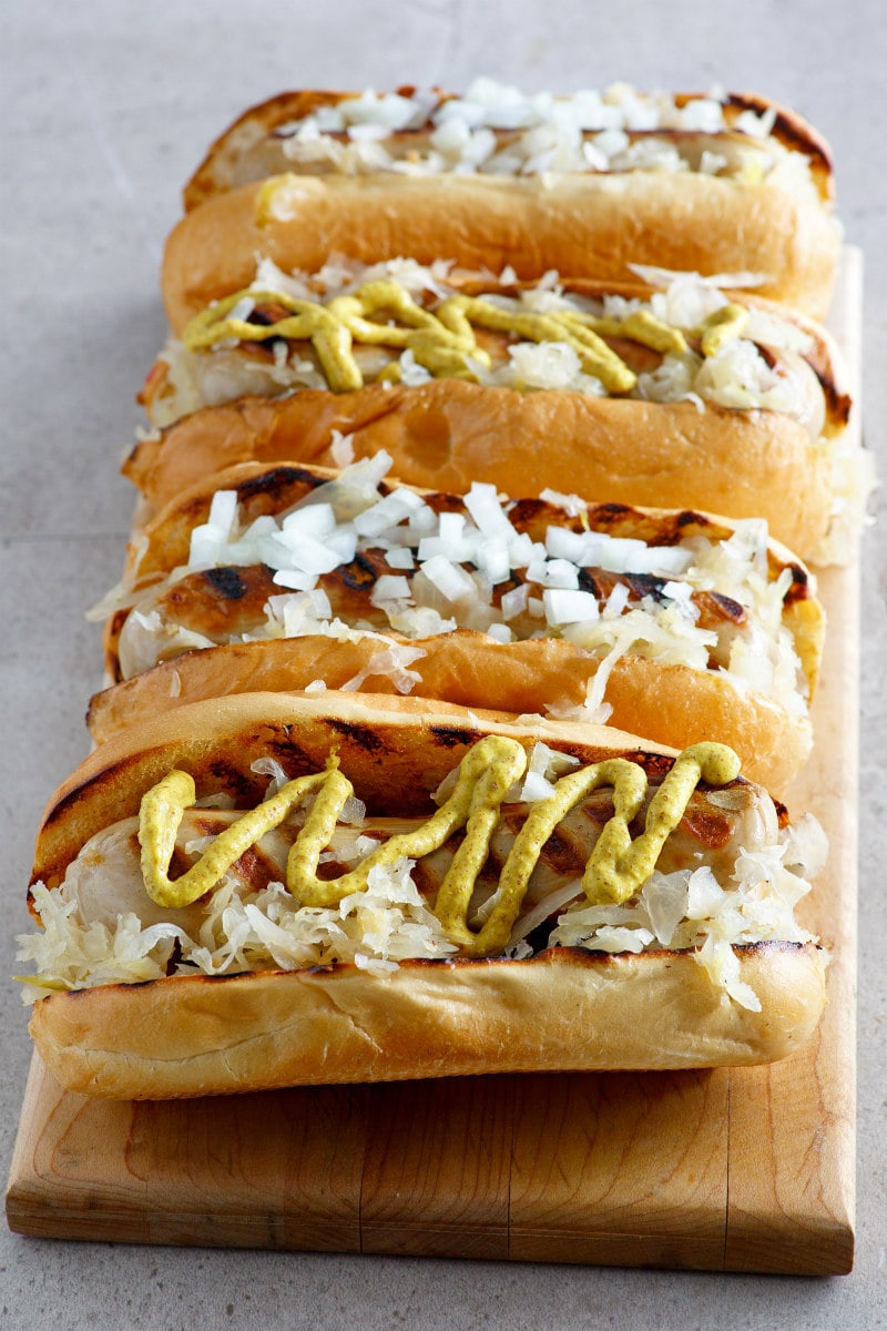 4 bratwurst Subs displayed on a cutting board topped with mustard or onion