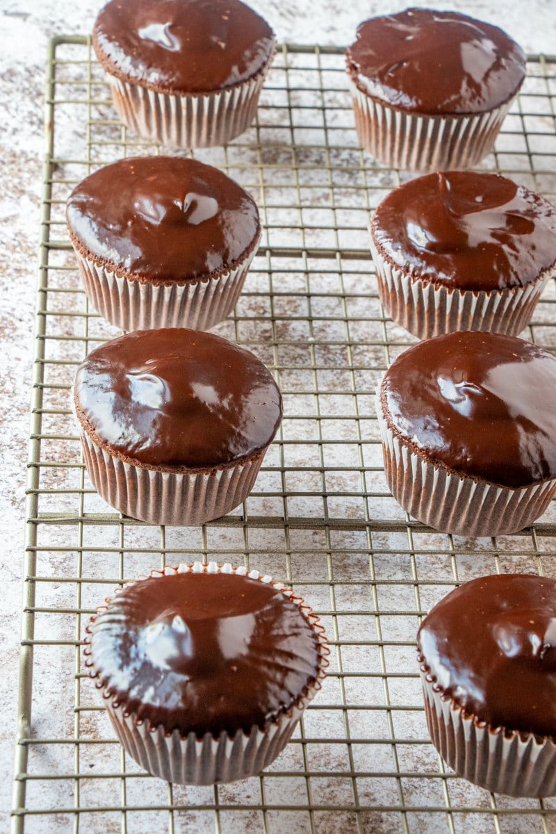 chocolate cupcakes dipped in ganache resting on cooling rack