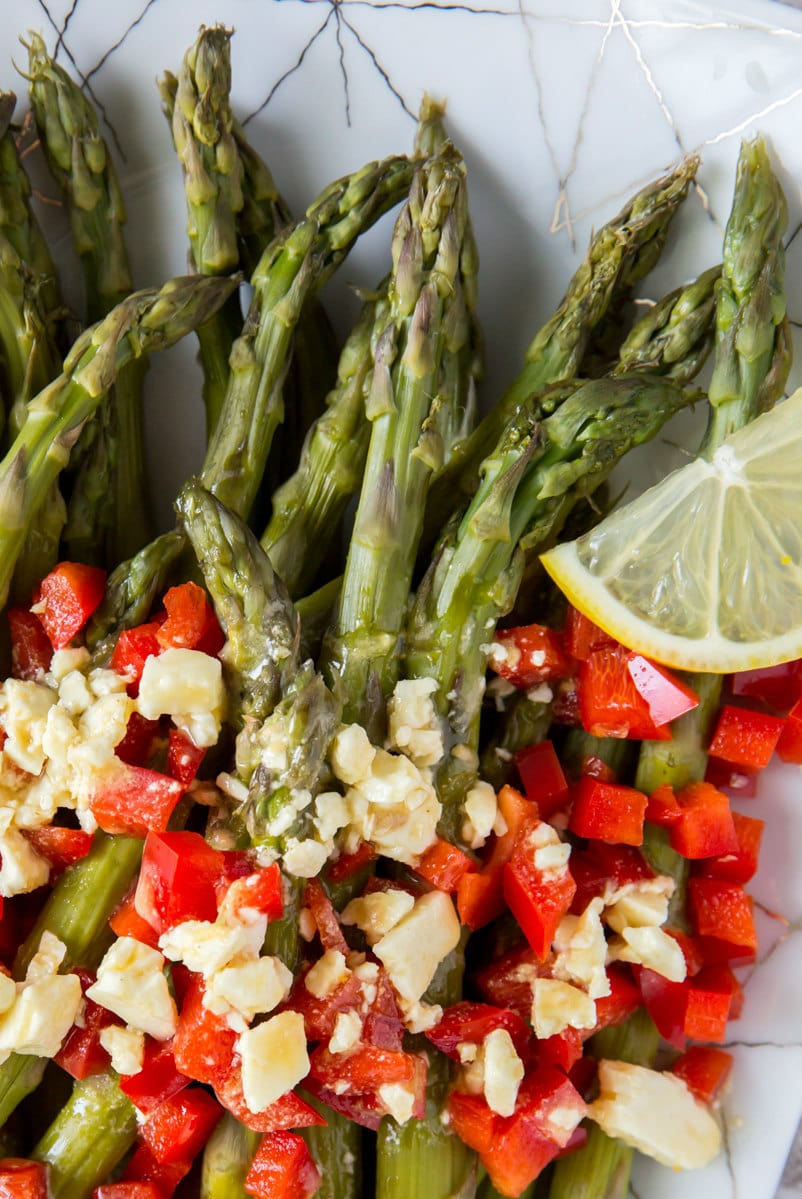 close up of chilled asparagus with feta vinaigrette and chopped red bell peppers and lemon slice