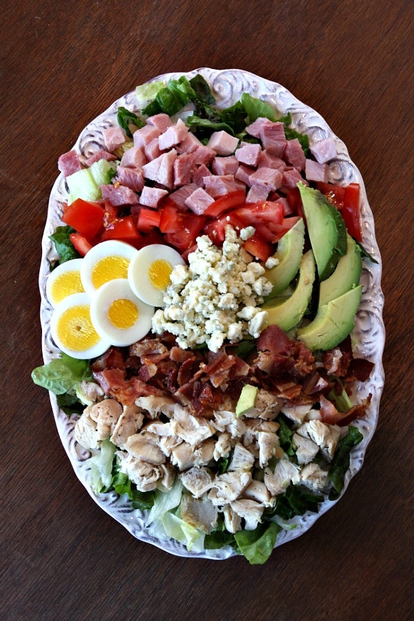 overhead shot of cobb salad on an oval white plate set on a wood table background