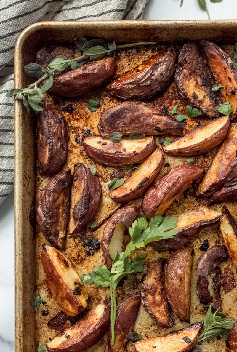 Greek Potato wedges on a baking sheet garnished with fresh oregano