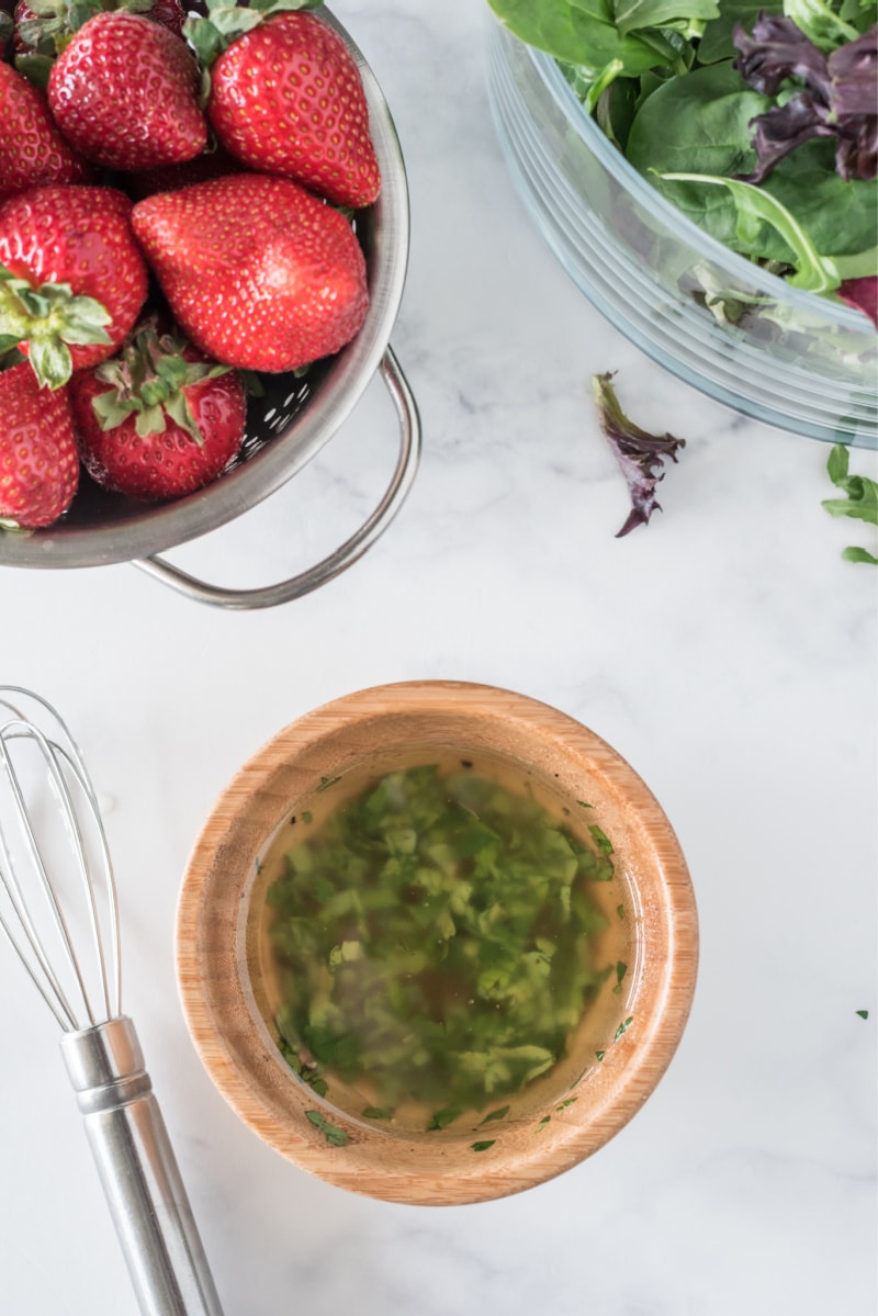 salad dressing with bowls of strawberries and greens on the side