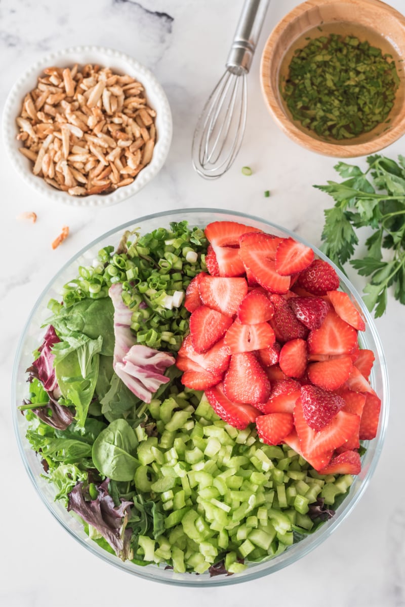bowl with ingredients for green salad with strawberries with dressing and sugared almonds on the side