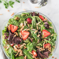 bowl of green salad with strawberries and sugared almonds