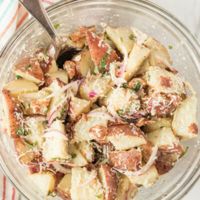 overhead shot of glass bowl with lemon basil roasted potato salad with a spoon set on a striped cloth napkin