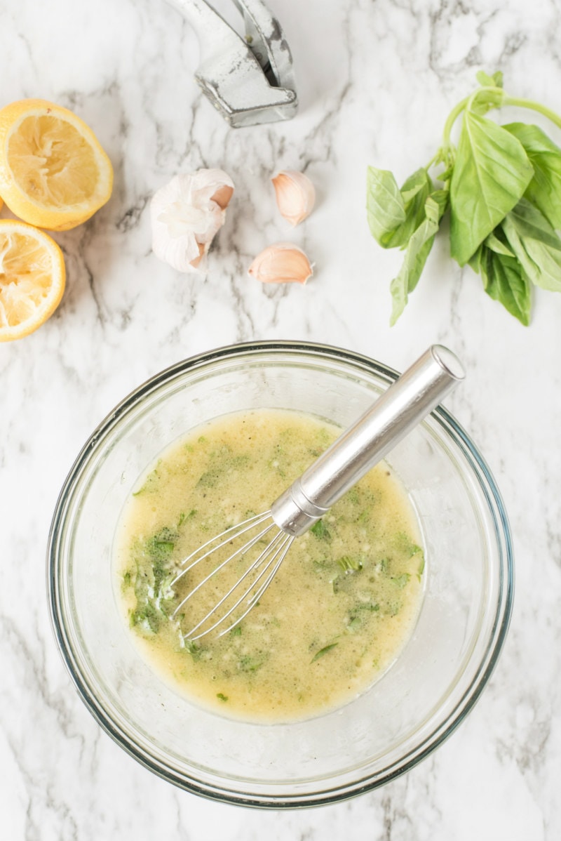 lemon basil dressing in a glass bowl with fresh basil, garlic and lemon