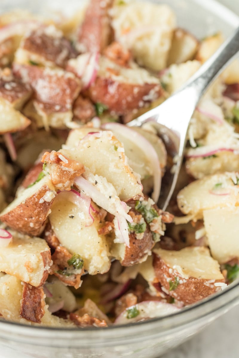 close up shot of lemon basil potato salad in a glass bowl with a spoonful of salad 