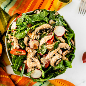 overhead shot of mandarin chicken spinach salad set on a bright striped cloth napkin