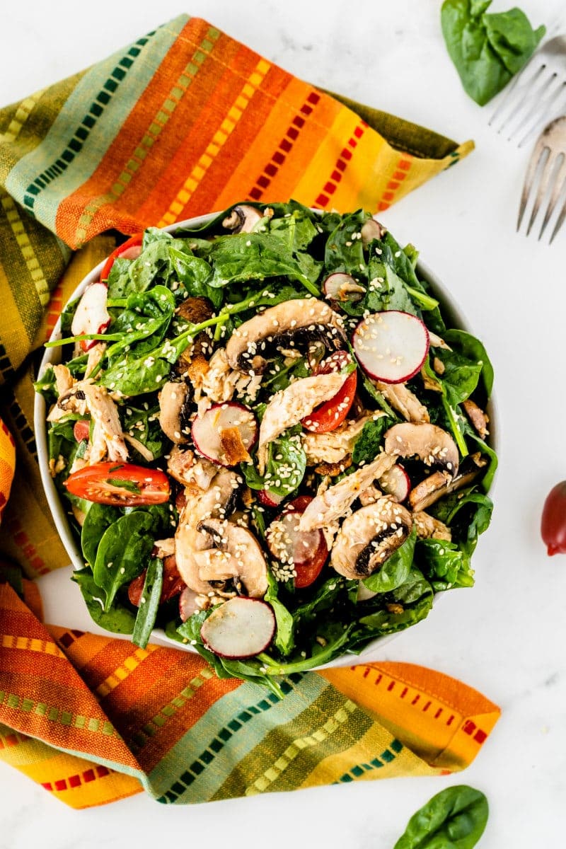 overhead shot of mandarin chicken spinach salad set on a bright striped cloth napkin