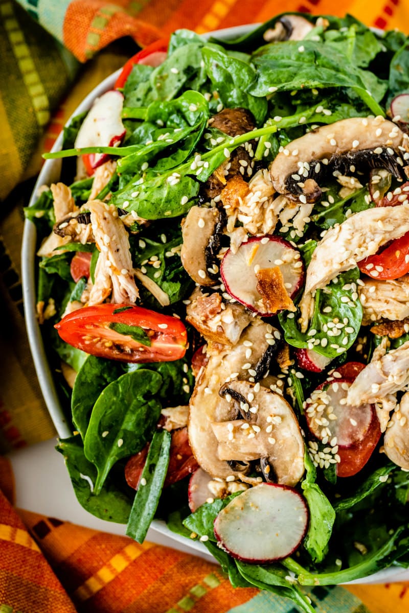 overhead shot close up of mandarin chicken spinach salad in a serving bowl set on top of a very bright and colorful cloth napkin