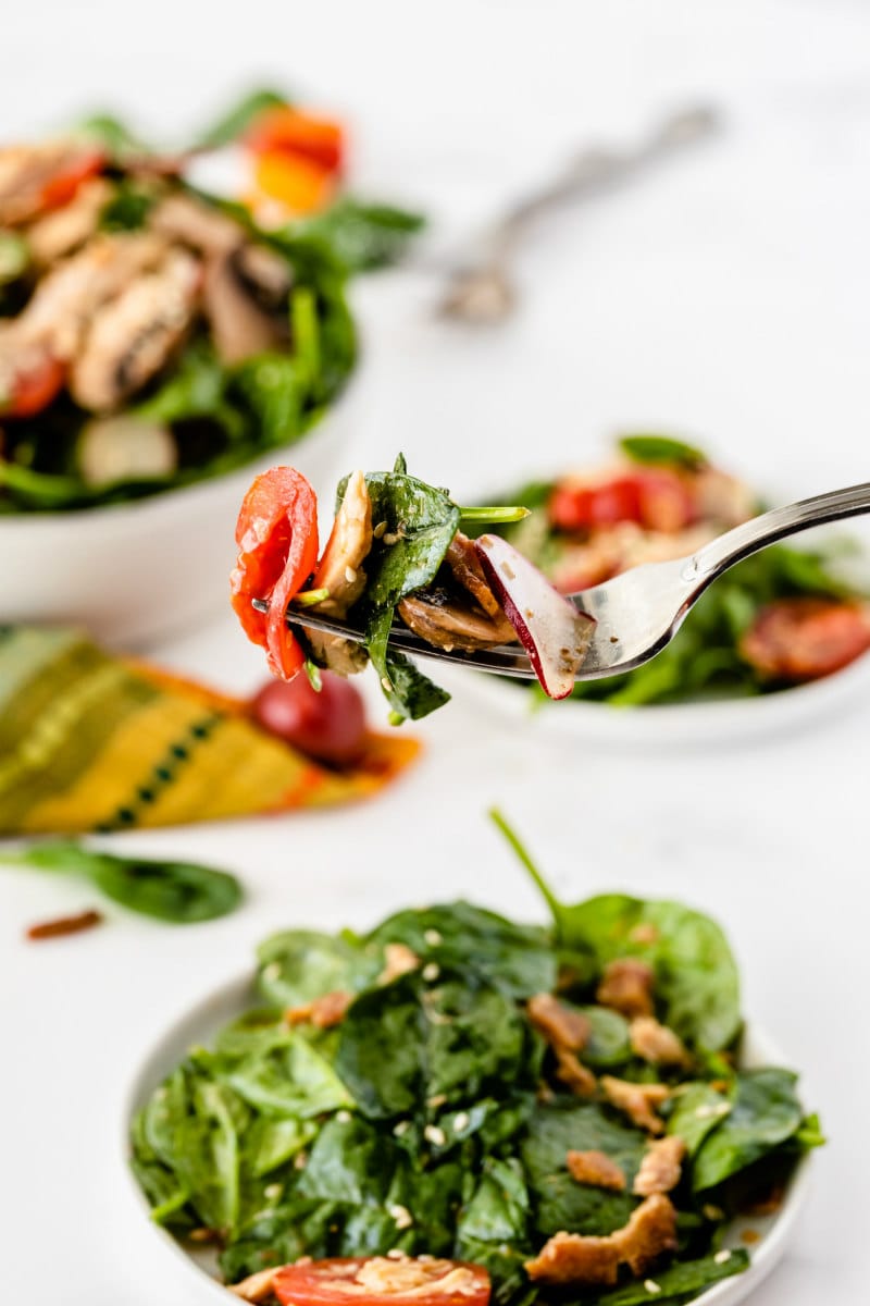 forkful of mandarin chicken spinach salad above plates of salad