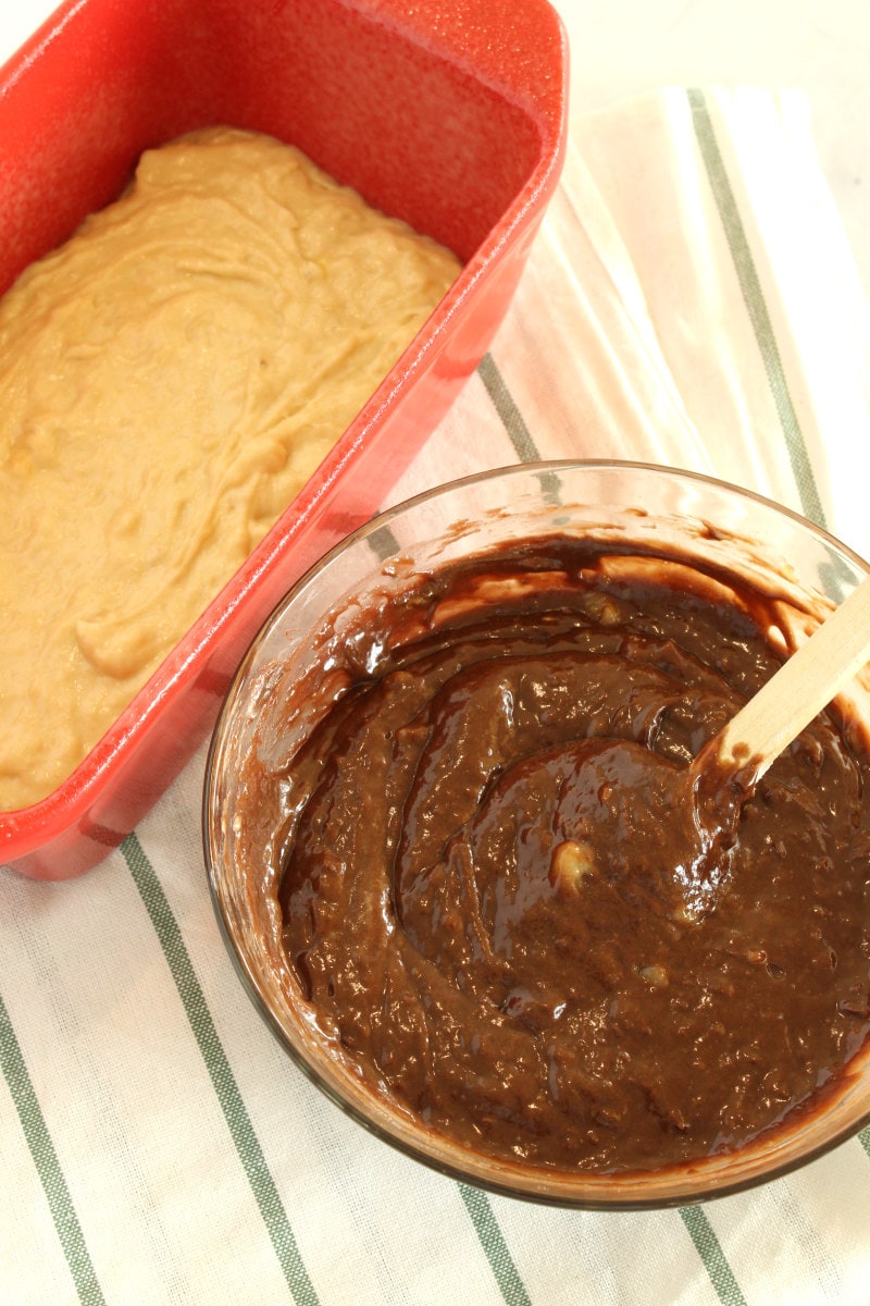 making banana bread with banana batter in a red loaf pan and chocolate batter in bowl next to it