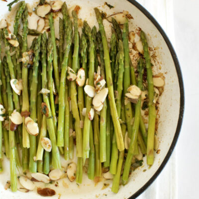 overhead shot of asparagus and almond butter in a white enamel skillet set on a white napkin with blue stripes