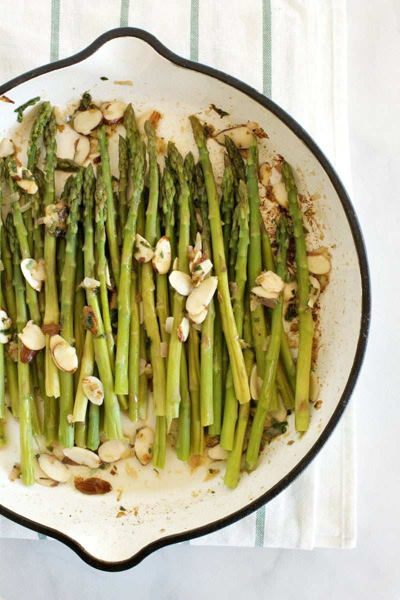 overhead shot of asparagus and almond butter in a white enamel skillet set on a white napkin with blue stripes