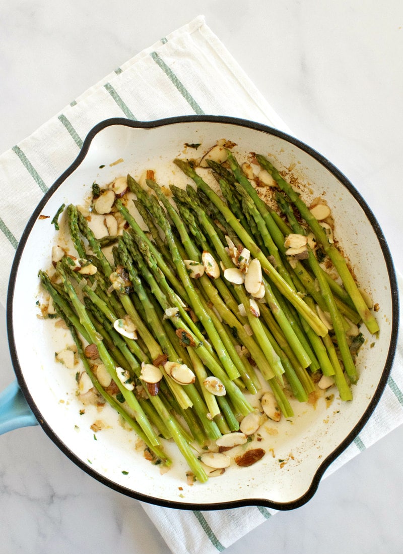 overhead shot of asparagus and almond butter in a white enamel skillet set on a white napkin with blue stripes