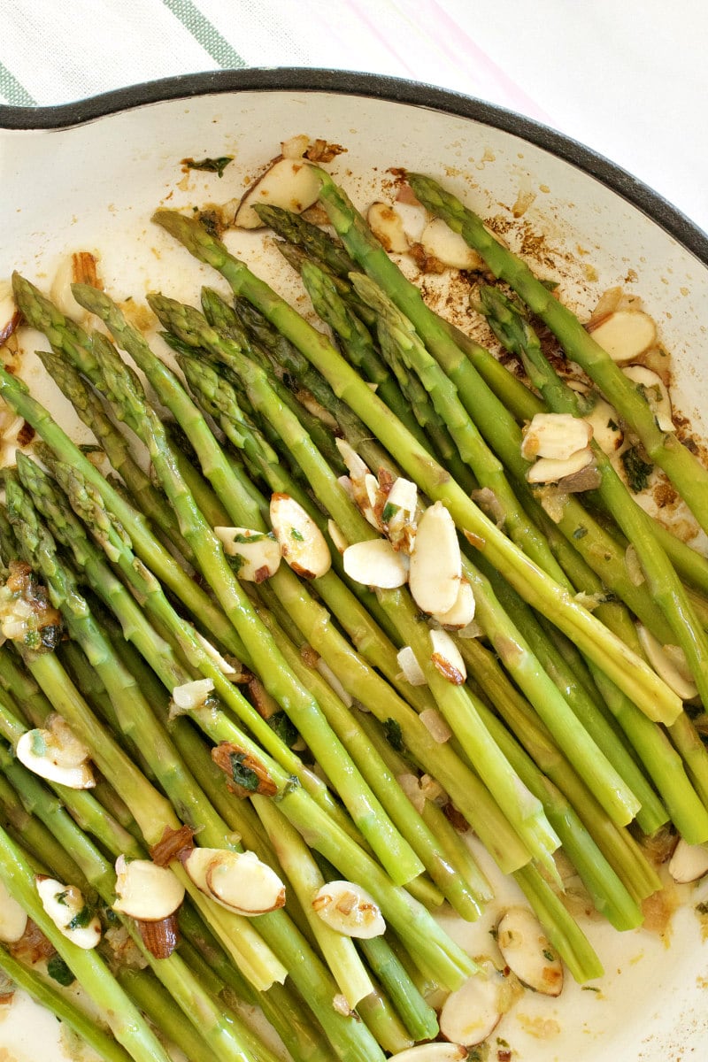 overhead shot of asparagus and almond butter being cooked in a white enamel skillet