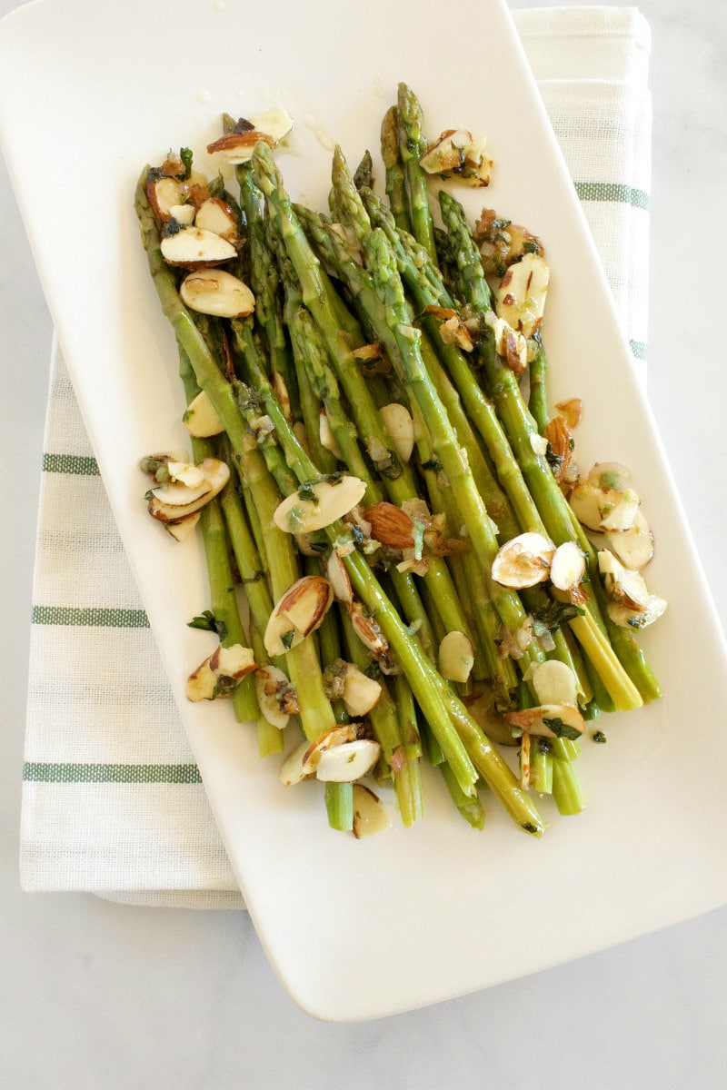 asparagus with almond butter displayed on a white platter and set on a white napkin with blue stripes