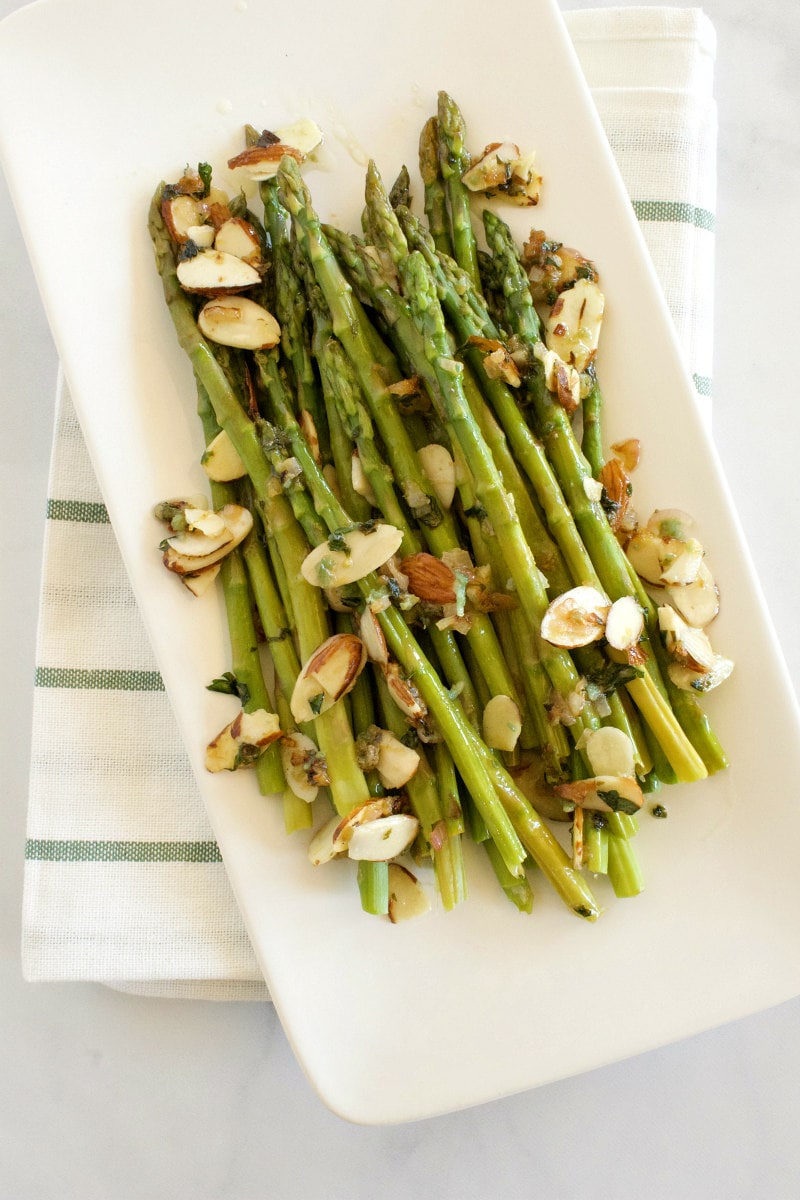 asparagus with almond butter displayed on a white platter and set on a white napkin with blue stripes