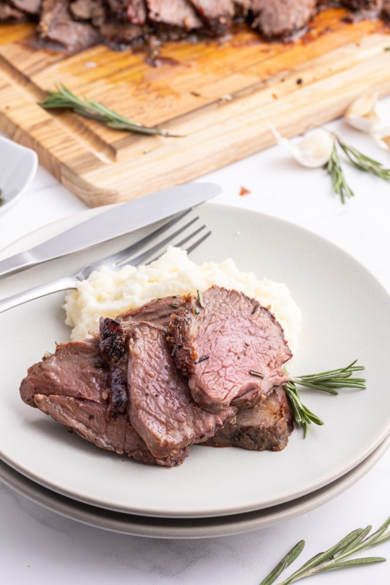 sliced leg of lamb on plate with fork and mashed potato