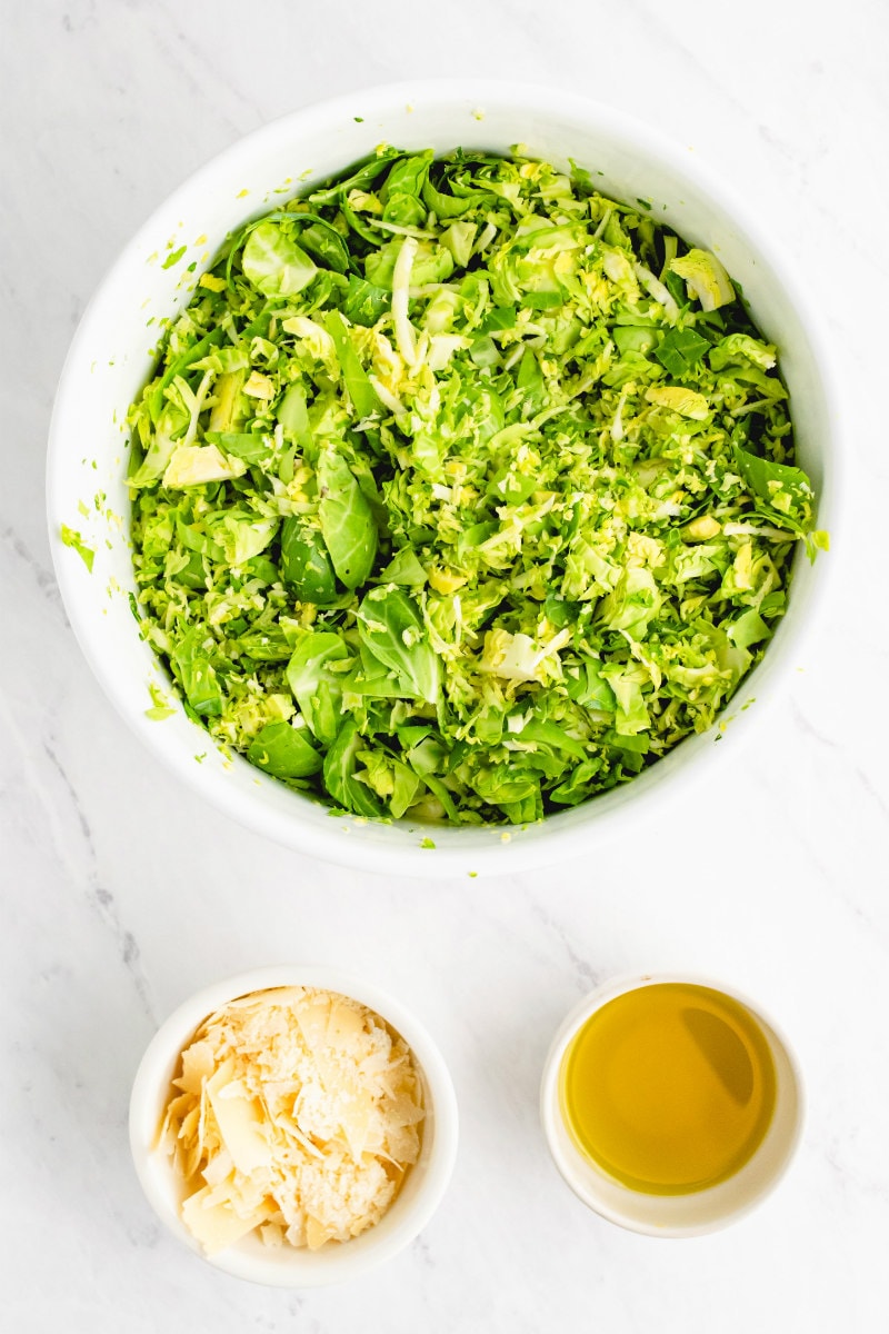 shredded brussels sprouts in bowl and parmesan and oil in bowls