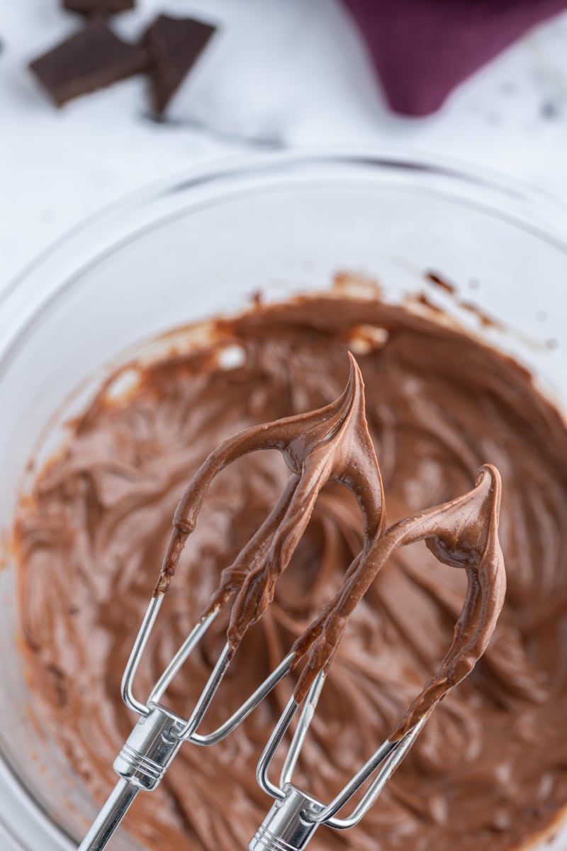 beaters with chocolate frosting over a bowl of frosting