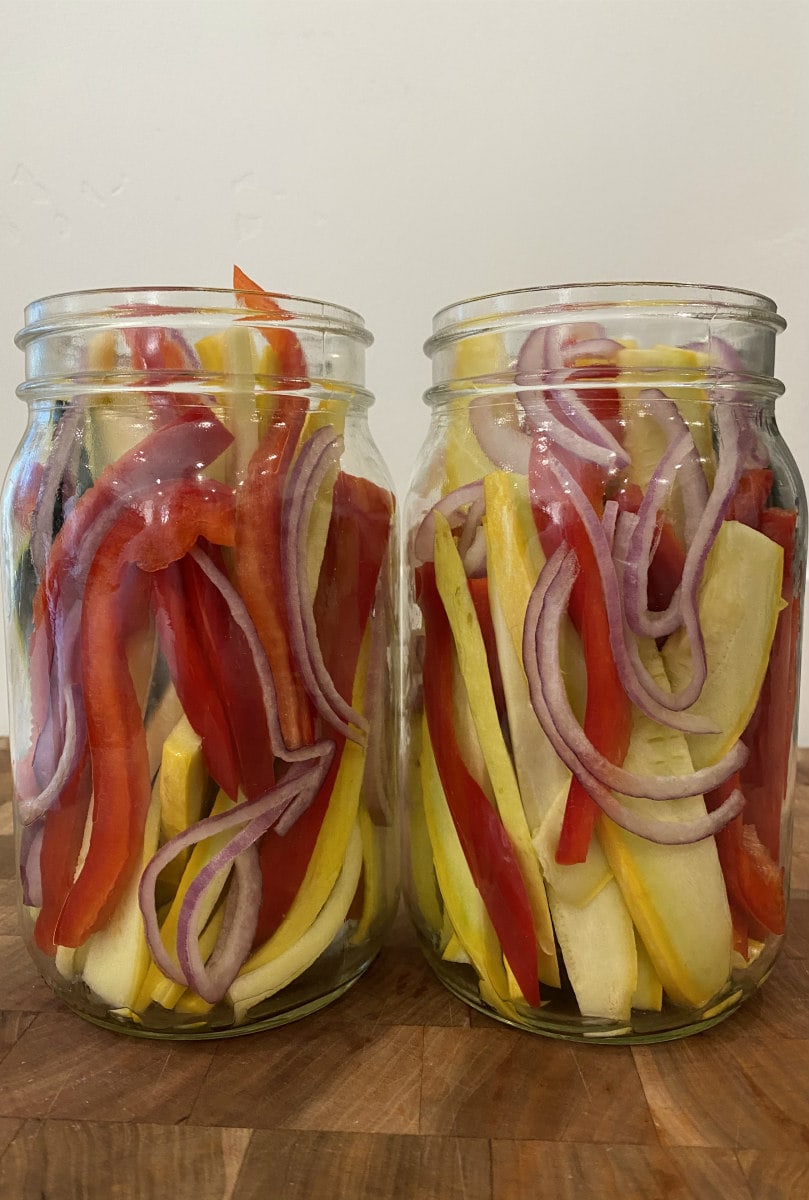 two open jars filled with sliced vegetables: red bell pepper, red onion, yellow squash and zucchini