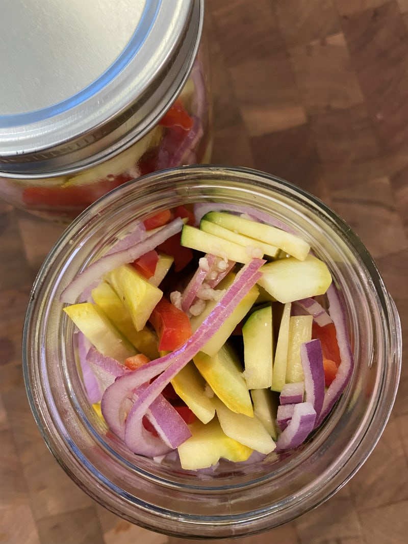 overhead shot looking into a jar that is marinating red onion, yellow squash, zucchini and red bell pepper