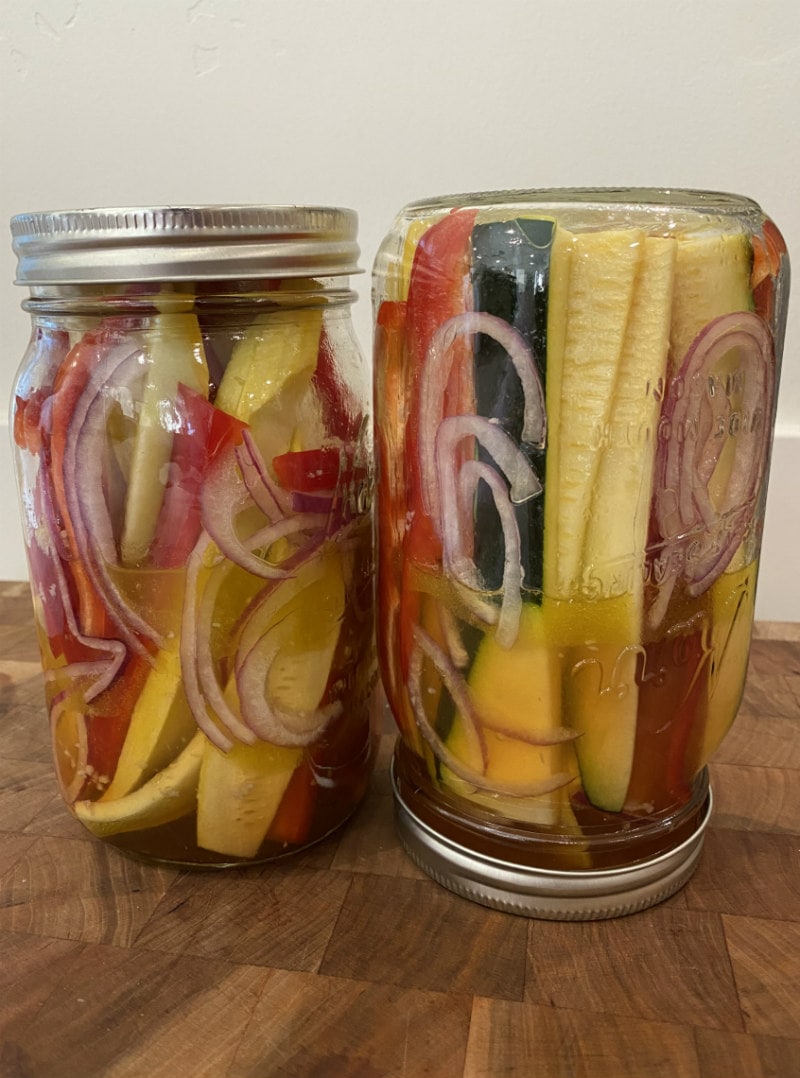 two jars marinating summer vegetables: yellow squash, red bell pepper, zucchini and red onion. one of the jars is turned upside down