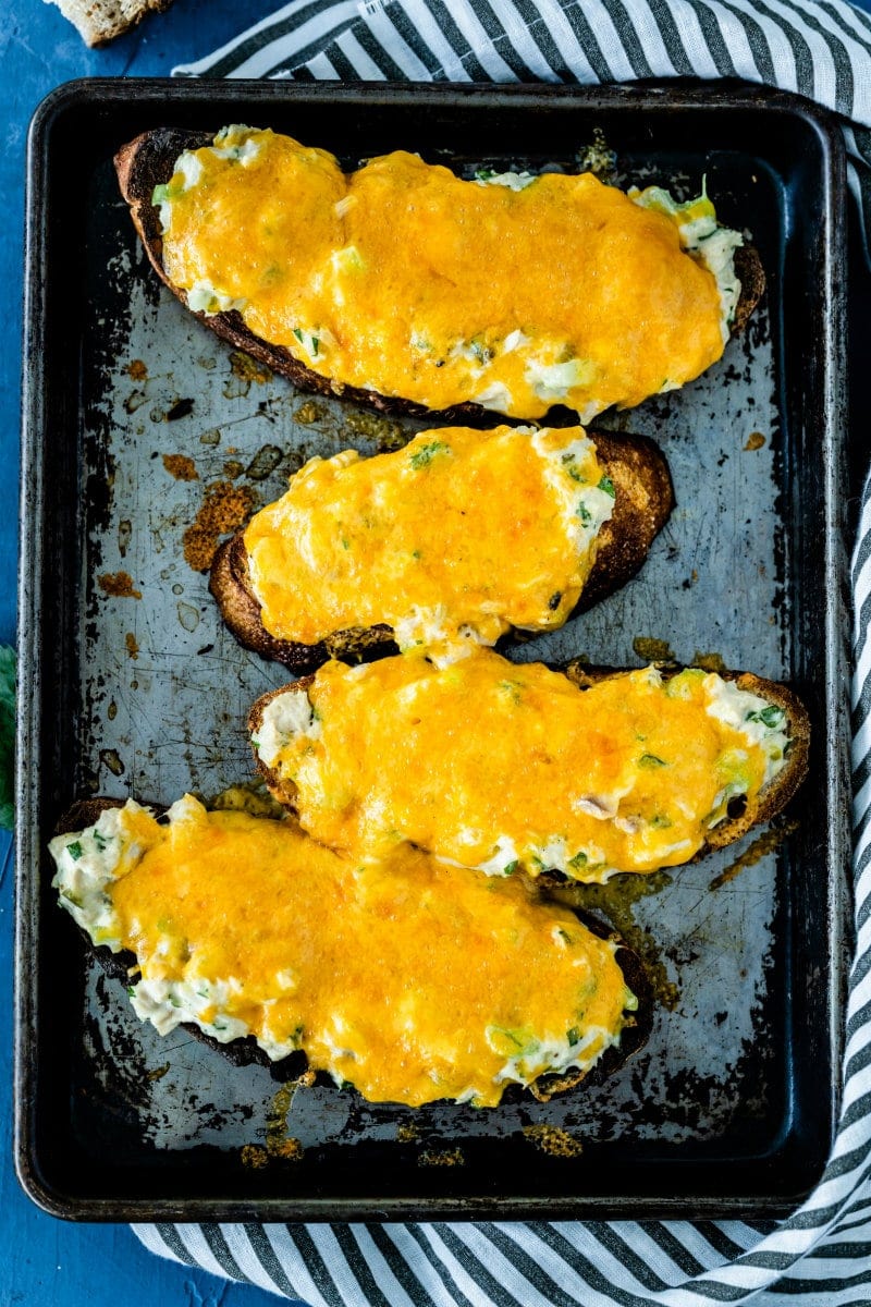 overhead shot of four tuna melts on a baking sheet set on a blue and white striped towel