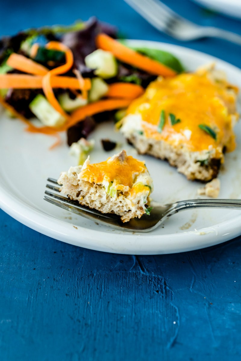 bit of a tuna melt on a fork with the rest of the tuna melt on a white plate with salad