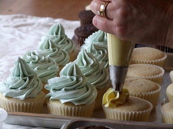 Frosting white cupcakes with green and yellow frosting