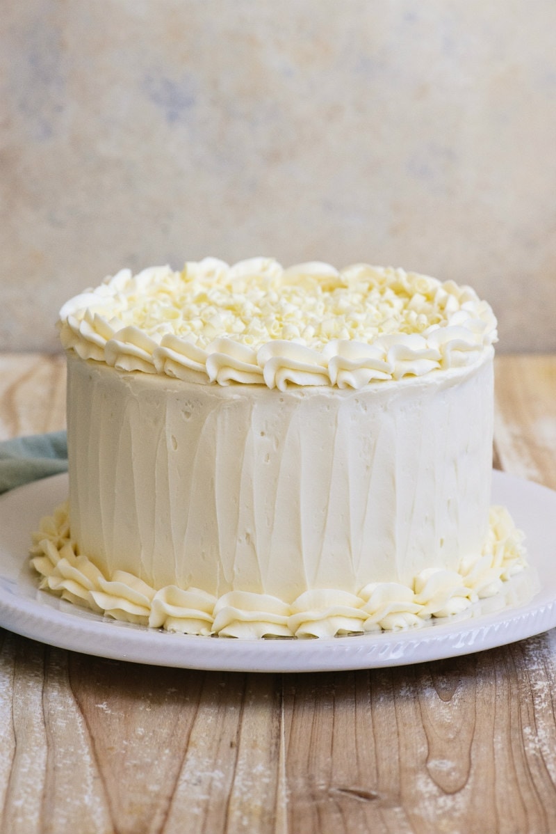 White Wedding Cake sitting on a white platter on a wooden board