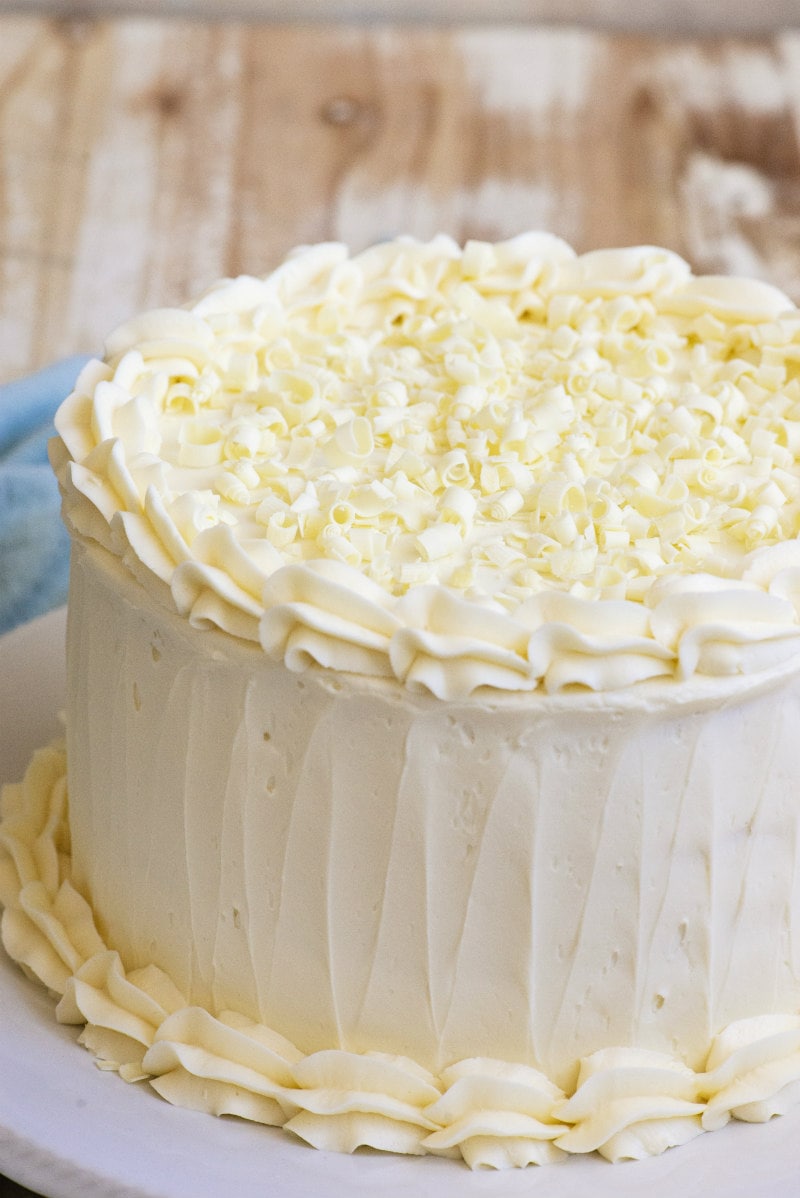 White Wedding Cake sitting on a white platter on a wooden board