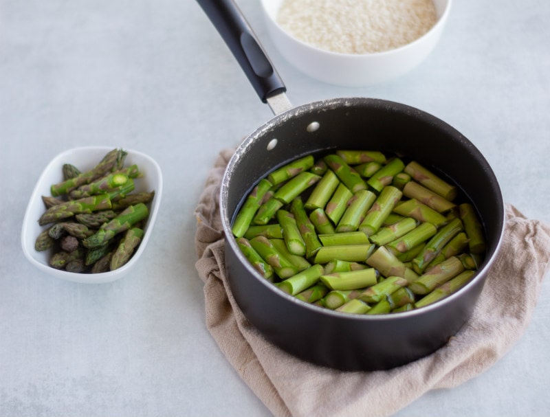 saucepan with water and asparagus pieces in it and a bowl of tips on the side