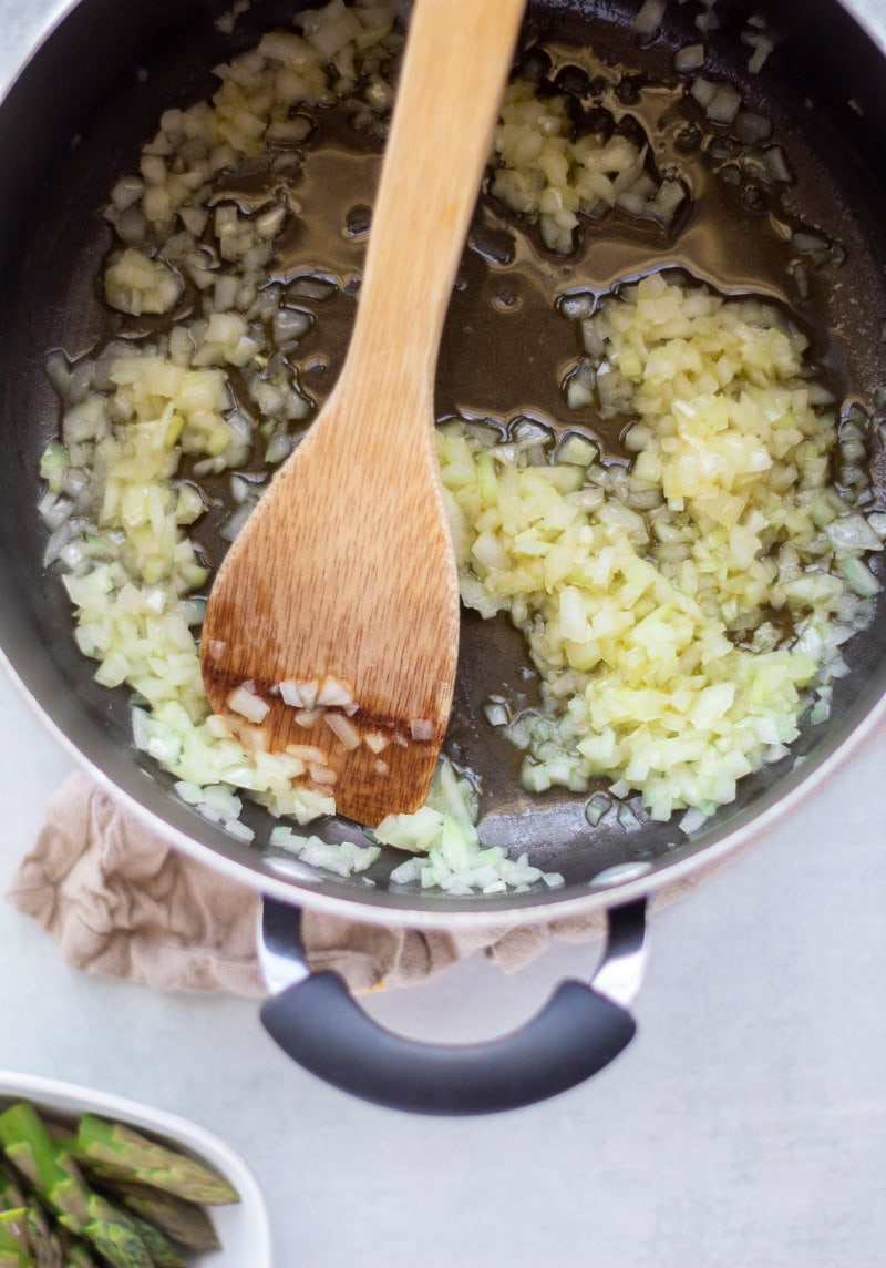 onion being cooked in pan with wooden spoon