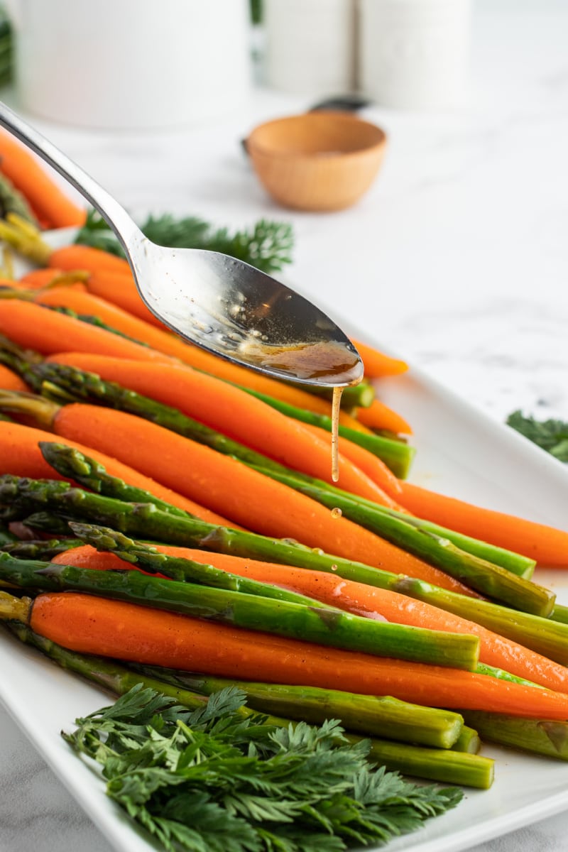 spooning maple butter sauce on carrots and asparagus