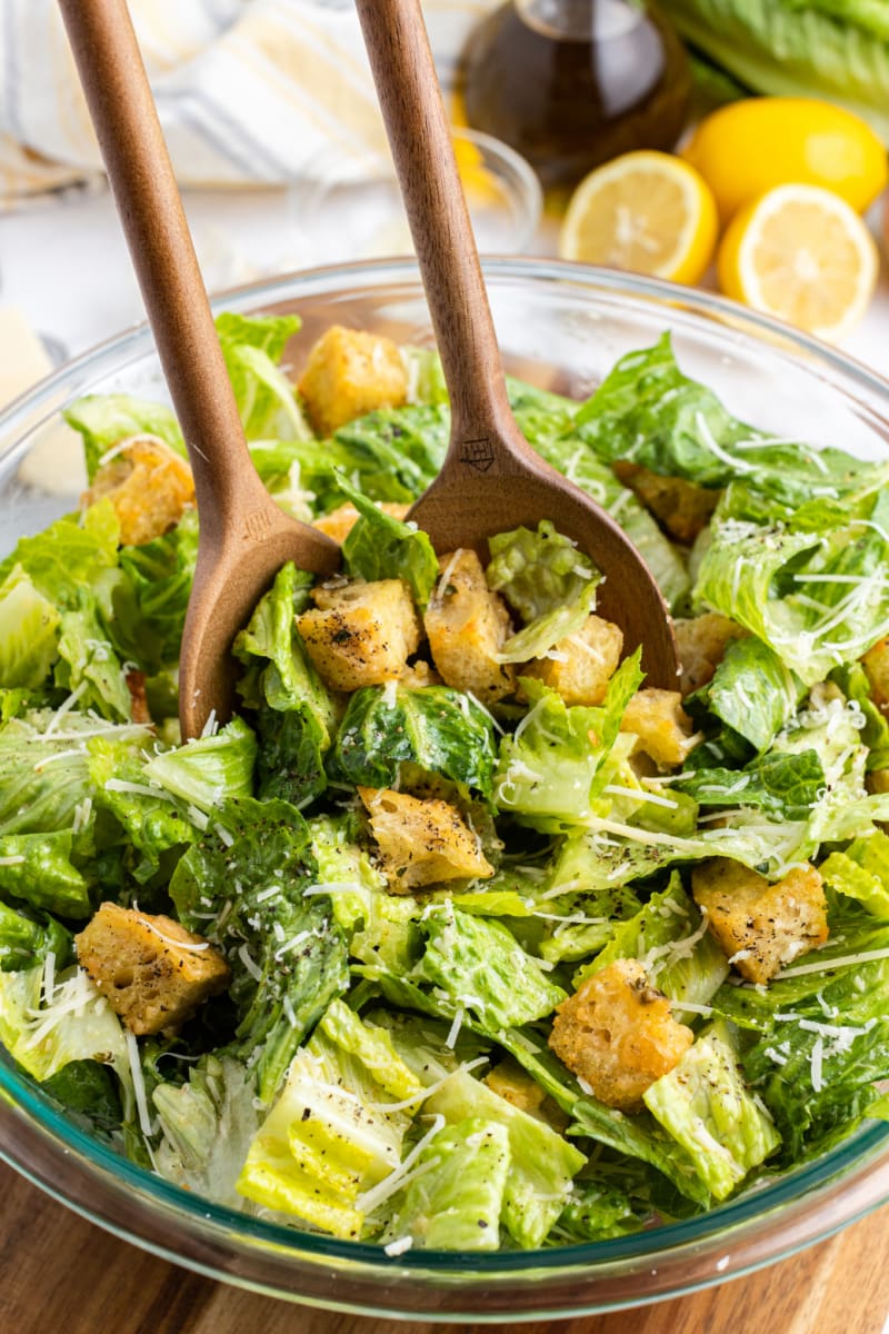 caesar salad with homemade sourdough croutons tongs tossing salad in bowl