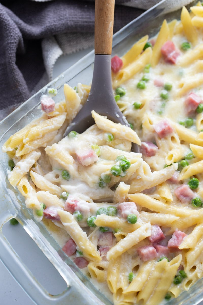 spooning cheesy baked penne out of casserole dish