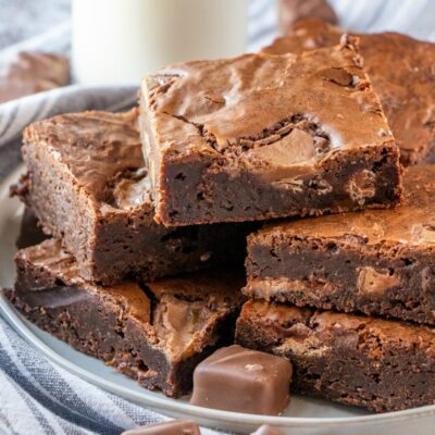 stack of milky way brownies on a plate with a glass of milk in the background- all on a striped blue and white napkin