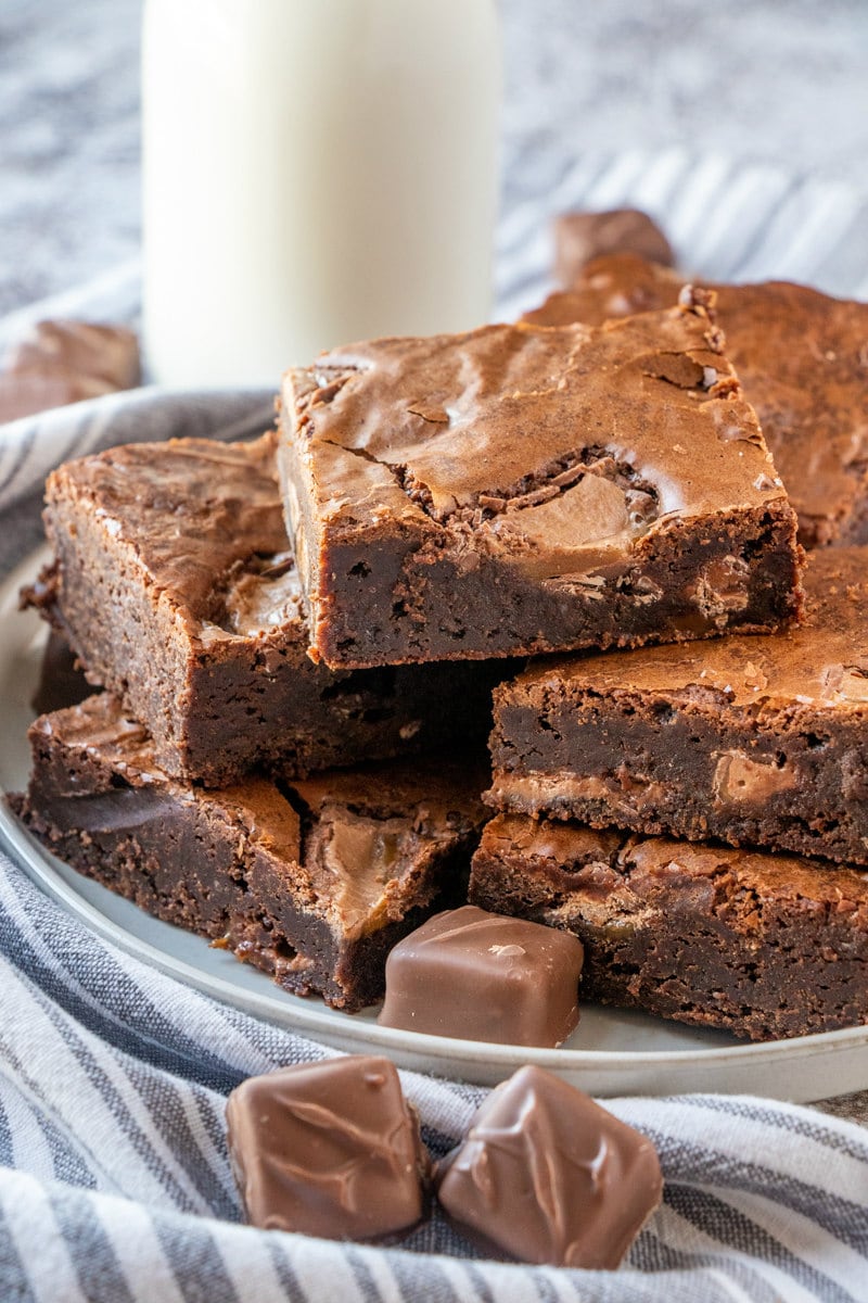 stack of milky way brownies on a plate with a glass of milk in the background- all on a striped blue and white napkin