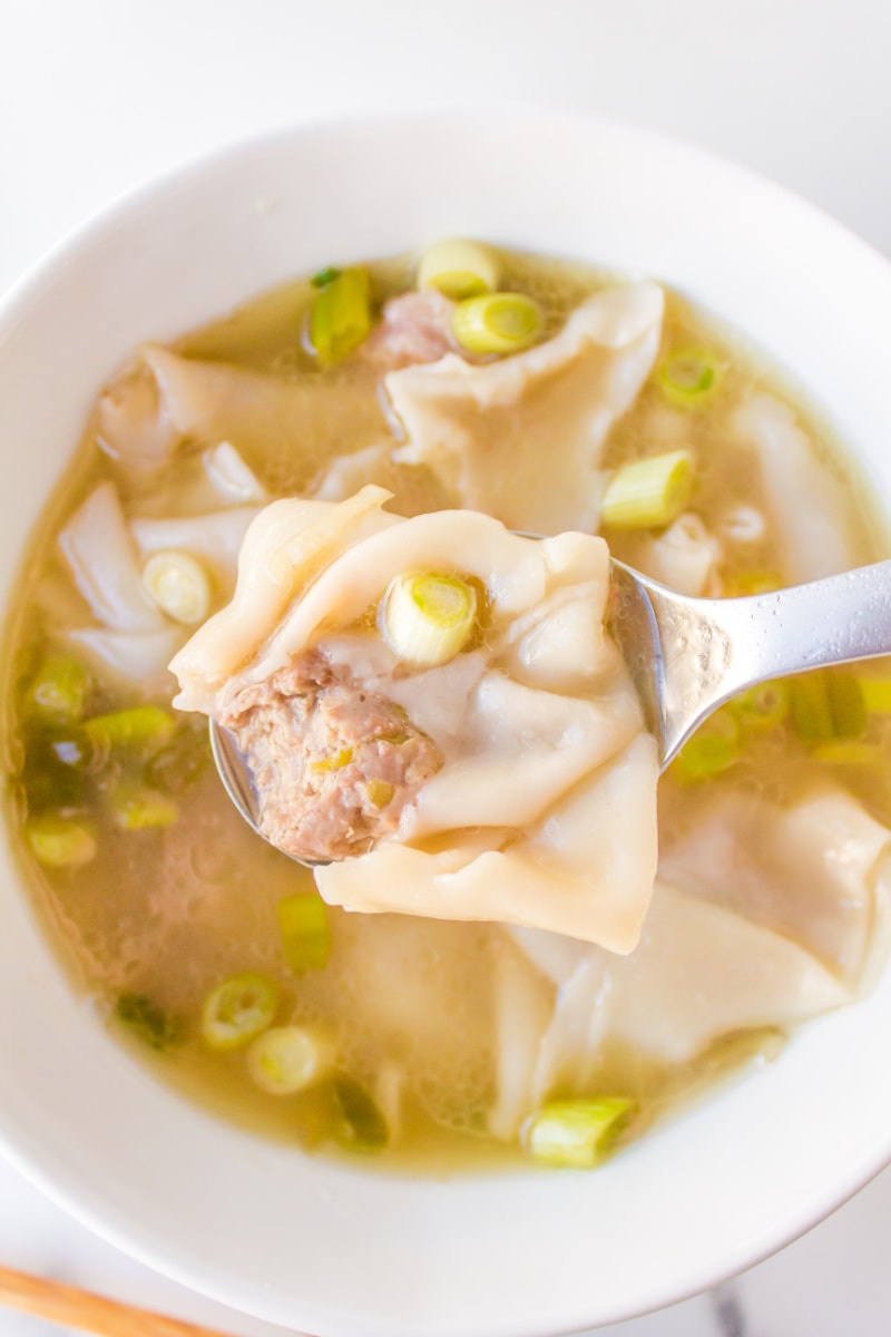 spoon holding wonton above wonton soup bowl