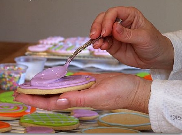 spooning royal icing onto sugar cookies